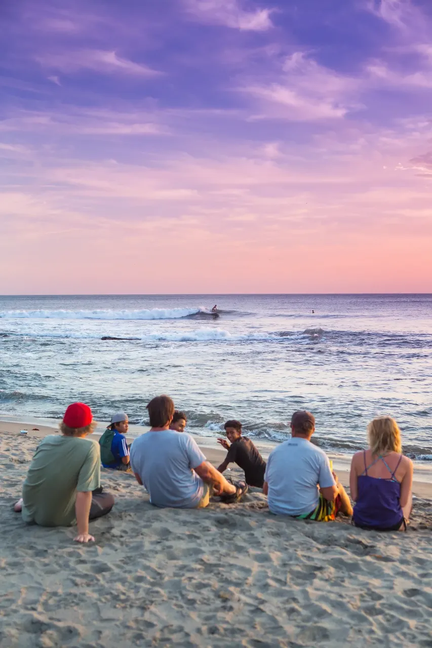Group of people sat on beach at Puerto Sandino at sunset — Getty Images