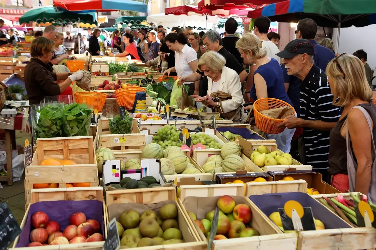O piață agricolă animată din Franța, cu tarabe pline de produse proaspete și bunătăți locale.