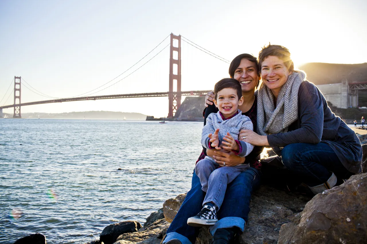 Lesbian family holding their toddler son on laps posing for a photo on San Francisco Bay, California, the US