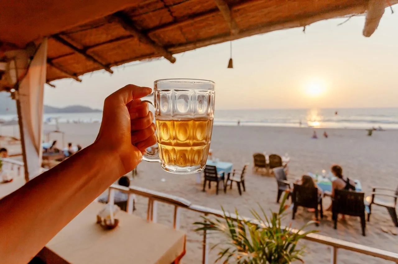 Beer mug in hand of tourist relaxing on a beach with lounge and some cafe outdoor of Asia