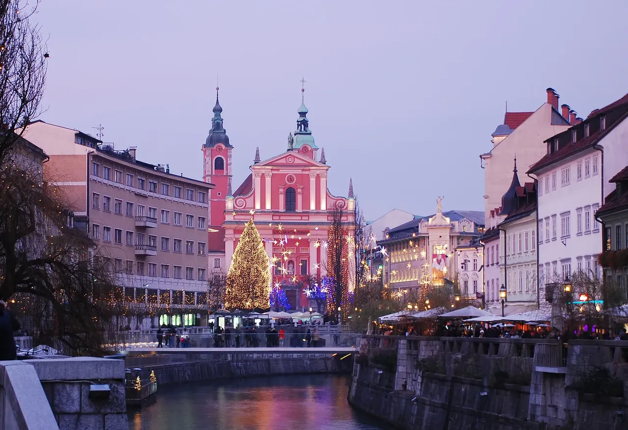 Ljubljana’s Christmas market illuminated at night, with the pink Franciscan Church in the background.