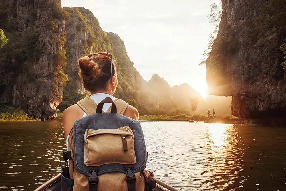 Woman with backpack sitting in a boat looking to the mountains in the sunset