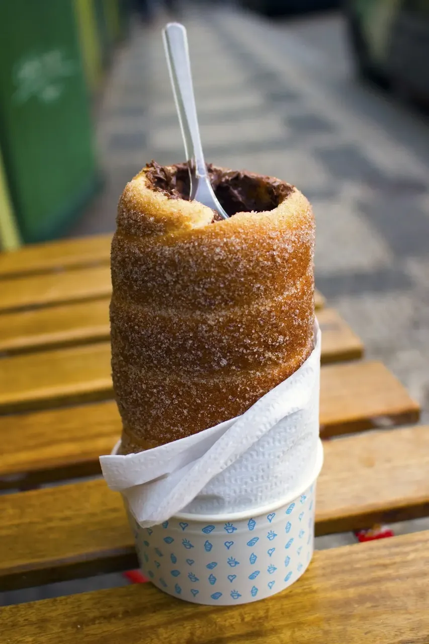 A sweet chimney cake coated in sugar, filled with chocolate, and served upright with a spoon