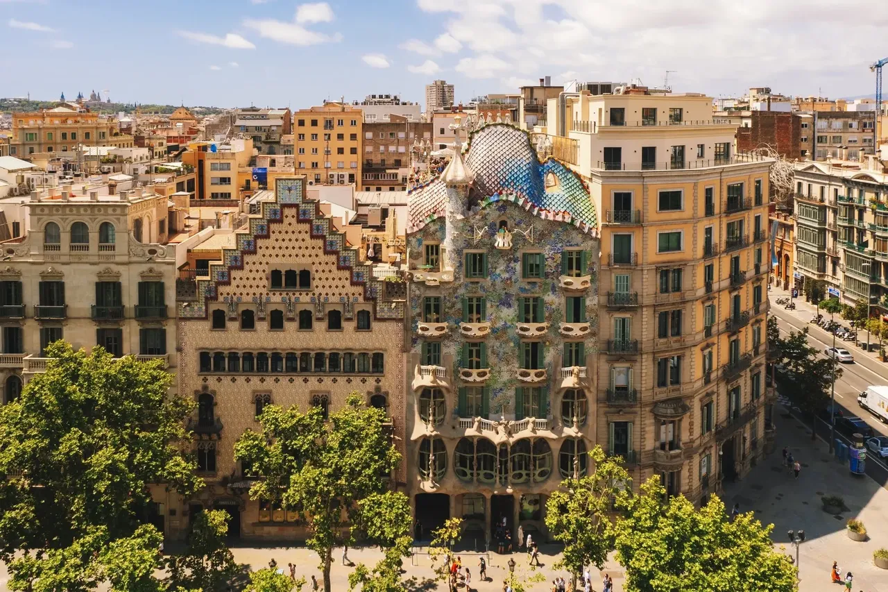 Fațada colorată și complexă a Casei Batlló din cartierul Gràcia, care etalează utilizarea emblematică de către Gaudí a mozaicurilor, formelor organice și designului arhitectural unic.