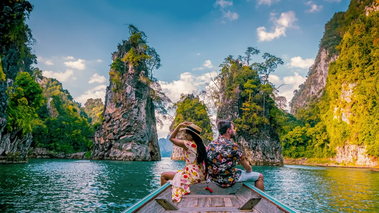 dvojice na typické thajské loďce se kochá výhledem na impozantní vápencové útesy na obrovském jezeře v národním parku Khao Sok, jezero Chiew Lan, Thajsko Surat Thani, muž a žena v přední části loďky