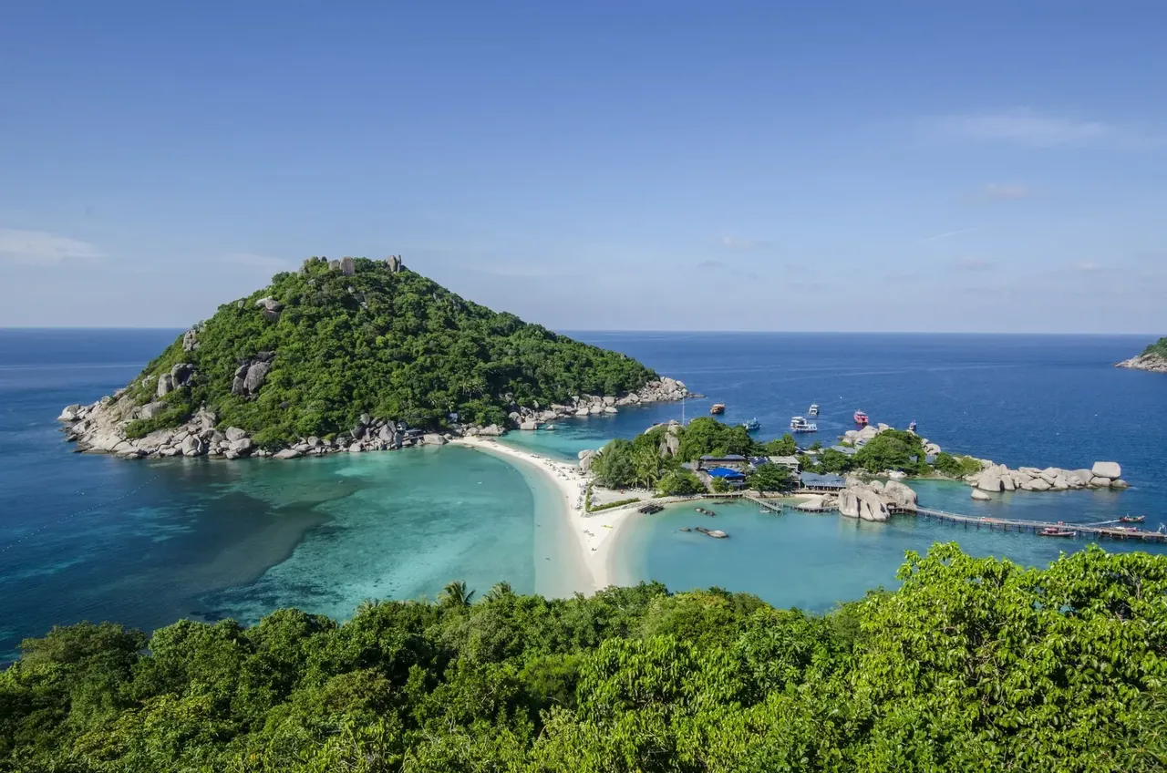 Vista panorámica desde la isla de Koh Tao, con vistas al mar azul verdoso y una isla cercana, con exuberantes colinas verdes y playas de arena.