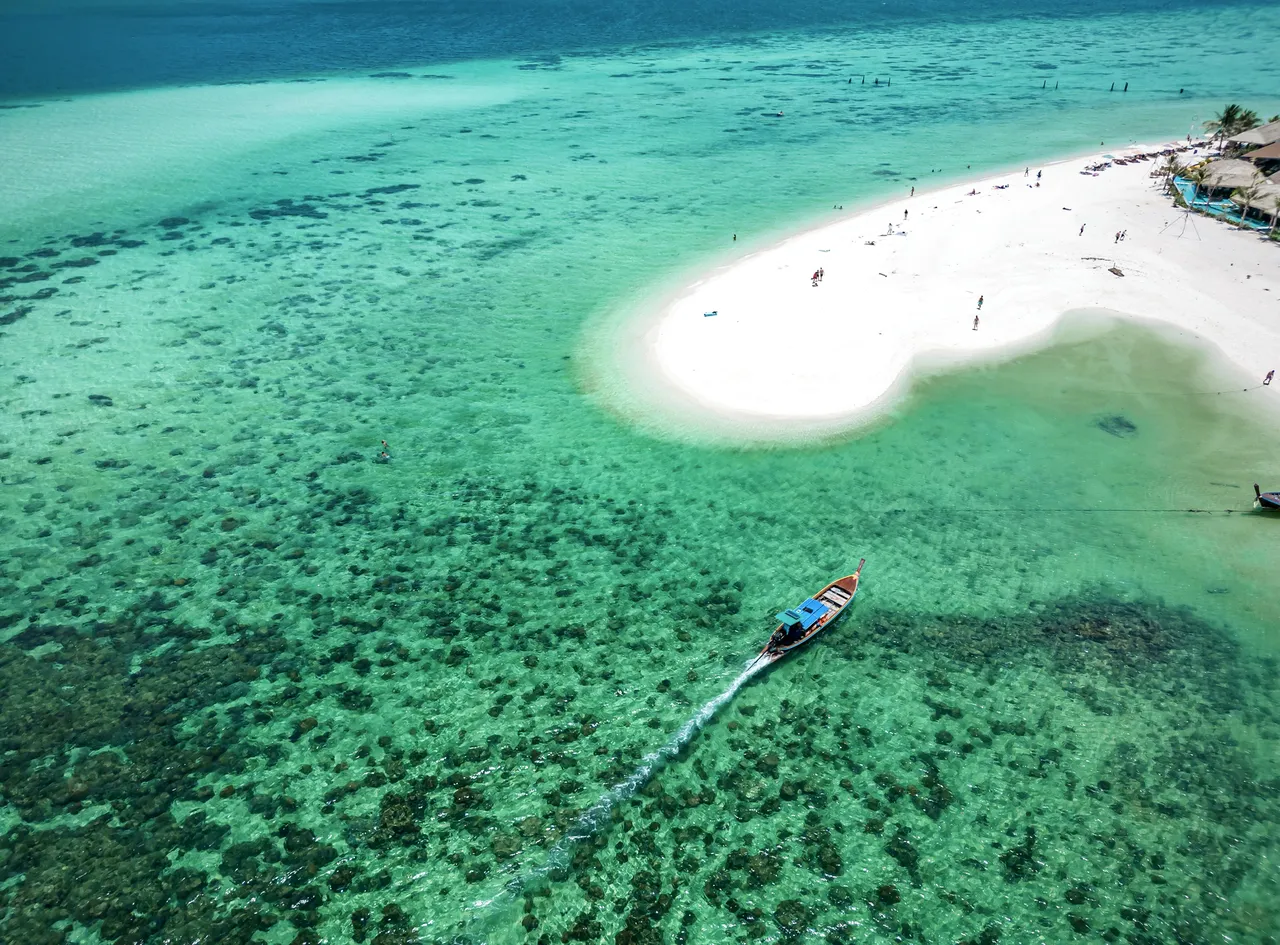 Pohled na pláž North Beach na ostrově Koh Lipe s jemným bílým pískem, křišťálově čistou tyrkysovou vodou, bujnými zelenými palmami a zářivě modrou oblohou