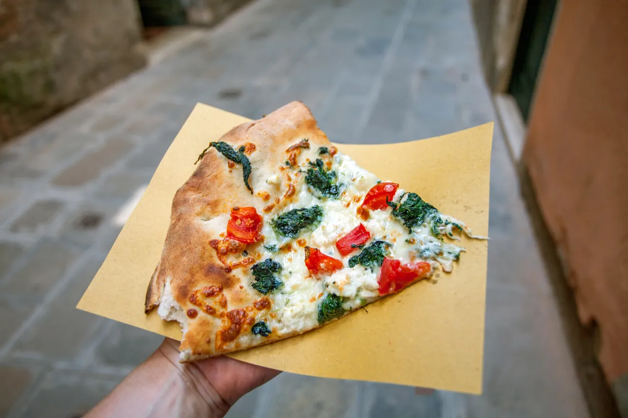 A slice of neapolitan style pizza in a hand outside in the streets of Venice.