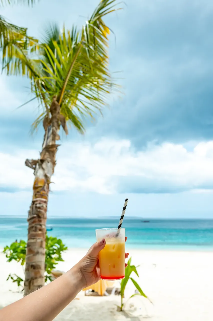 Hand holding cocktail against white-sand beach backdrop with palm tree — Getty Images