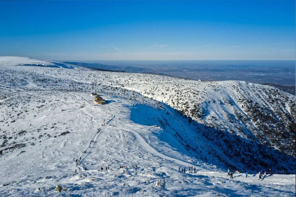 Pass under the Śnieżka Mountain. Tourists hiking on the mountain trail between Dom Śląski mountain chalet and Śnieżka Mountain in winter.