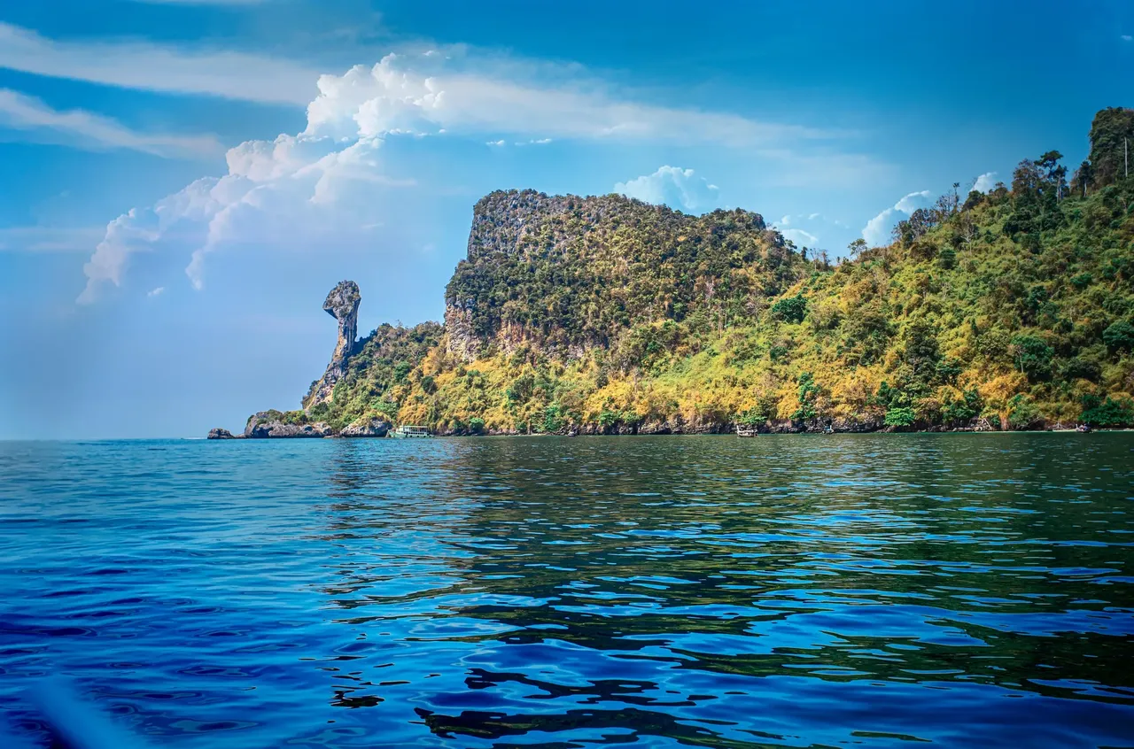 A small tropical island with a distinct rock formation resembling a chicken’s head, surrounded by clear turquoise waters and white sandy beaches.