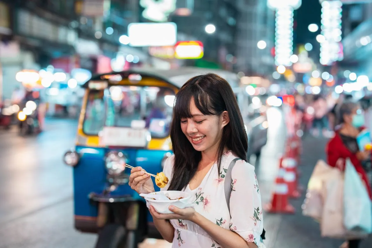 A young asian woman trying some food at night market in Bangkok, Thailand