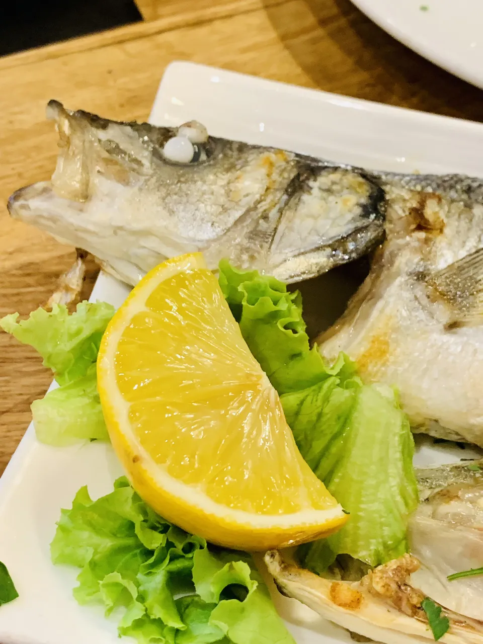 Záběr zblízka na grilovaného albánského mořského vlka ozdobeného salátem a klínkem citronu