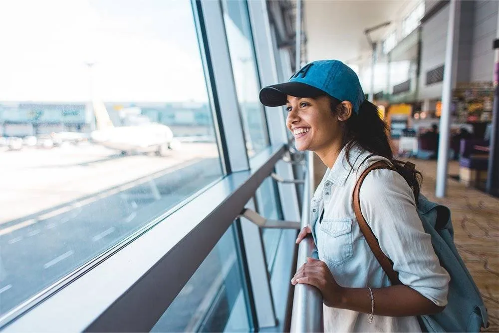 Girl looking out of an airport terminal window and smiling — Shutterstock