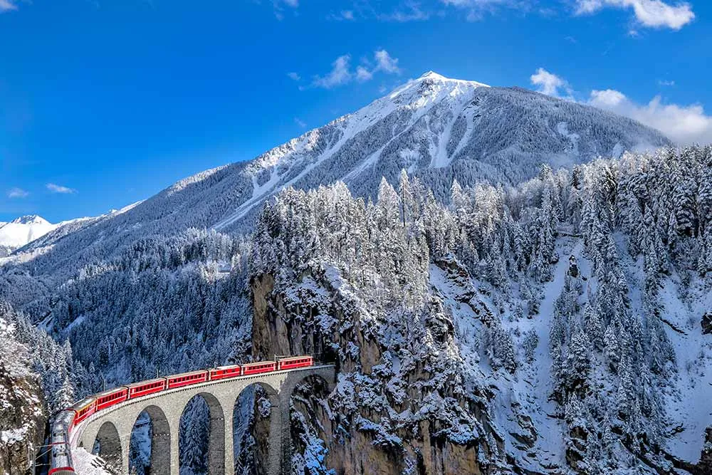 Švýcarská trať se vine oslnivou alpskou scenérií, po úzkých mostech přes infarktové rokle