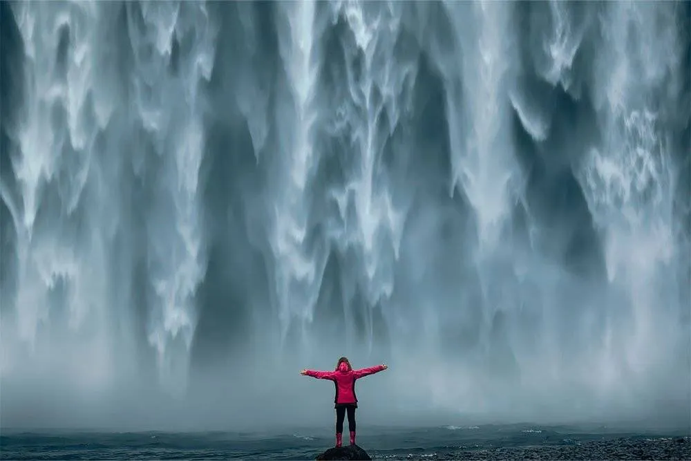 Person stood below and in front of a huge waterfall — Shutterstock