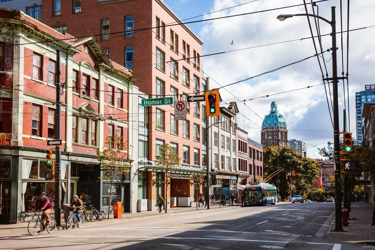 Una imagen de la animada Homer Street en Vancouver, con edificios históricos de ladrillo, ciclistas y la emblemática Torre del Sol al fondo
