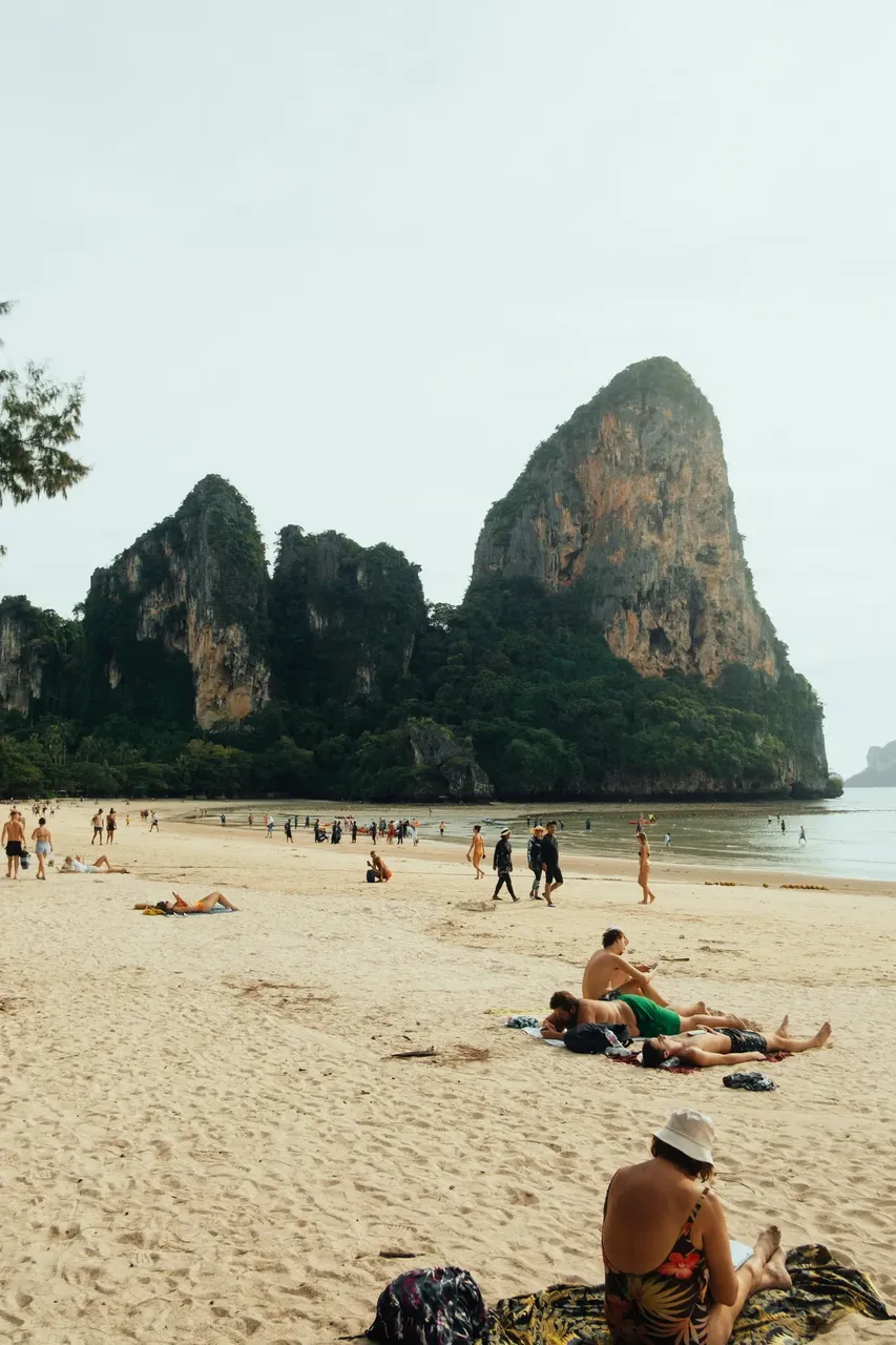 A stunning beach with soft white sand, framed by towering limestone cliffs and lush greenery, with calm, crystal-clear water gently lapping the shore.