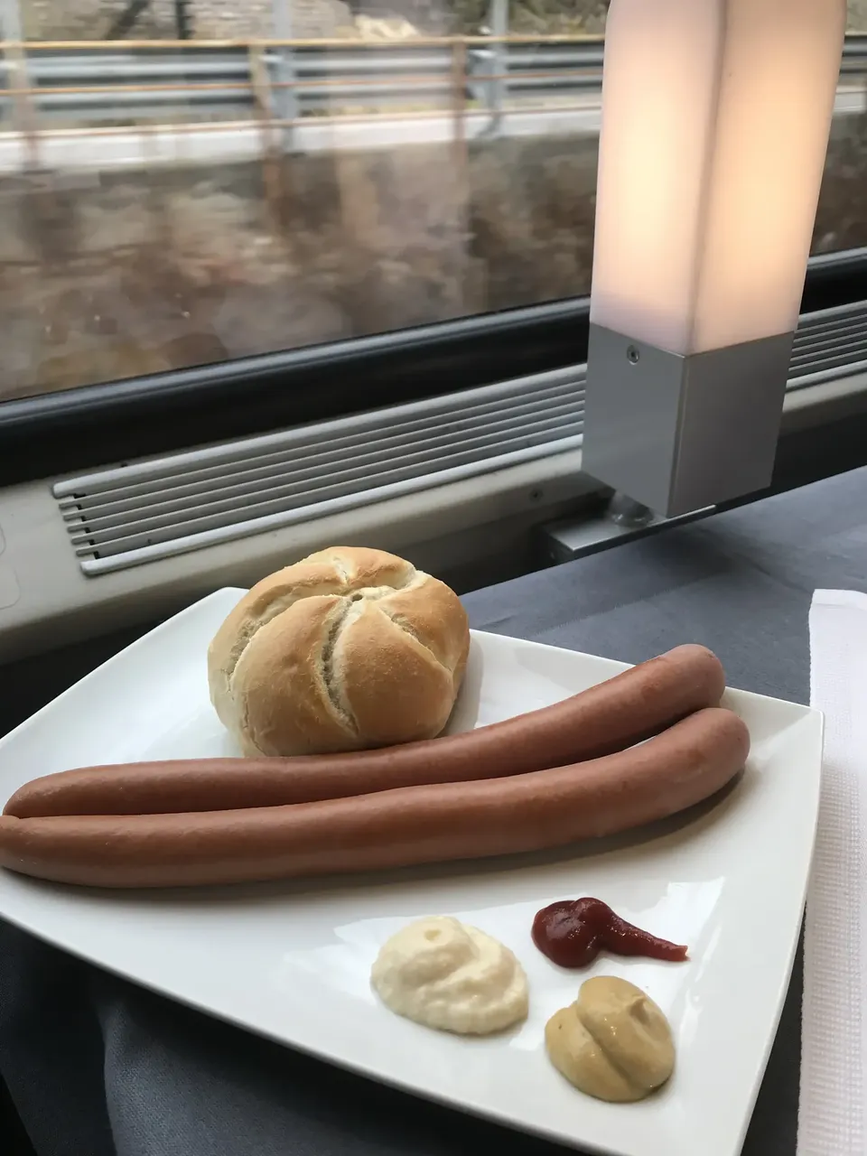Frankfurters and bread roll on a plate with sauces on train — Getty Images