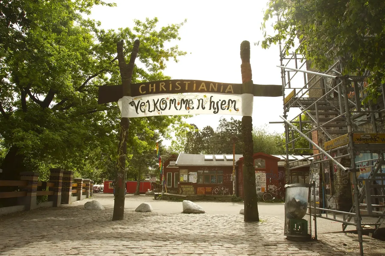 Dřevěná vstupní brána do kodaňské čtvrti Christiania s transparentem „Velkommen Hjem“ mezi stromy