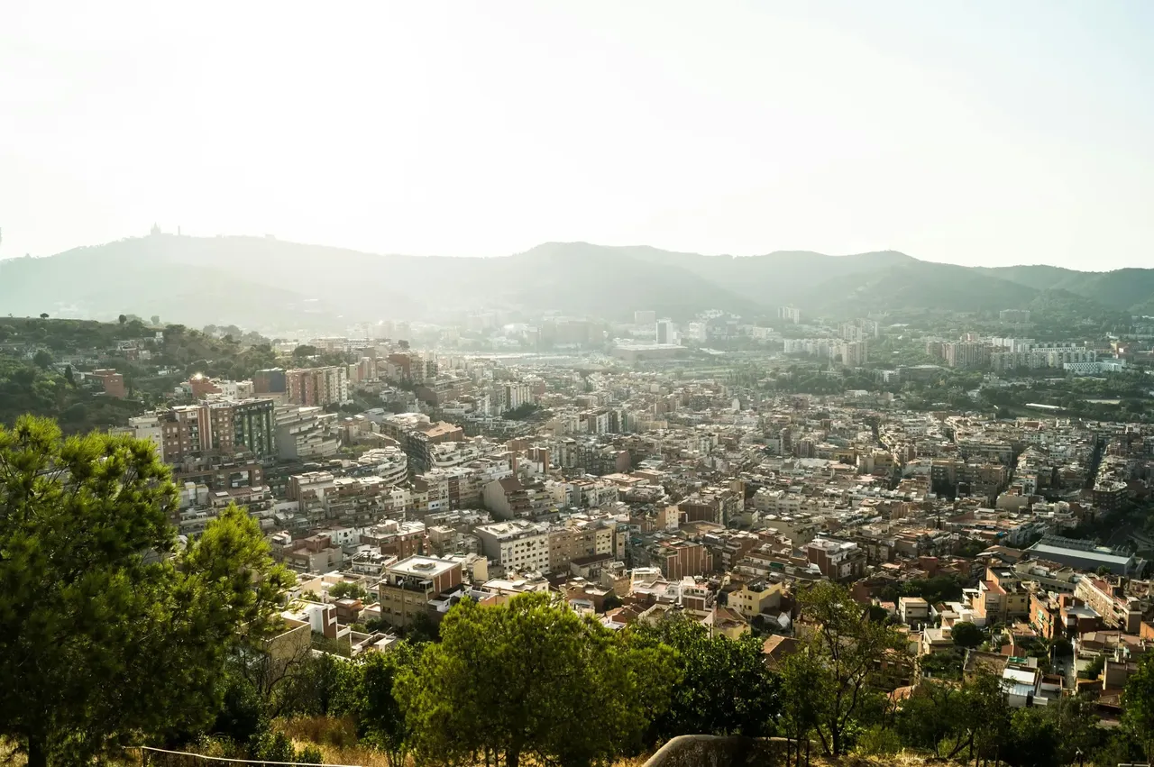 O vedere panoramică a Barcelonei de la Buncărele del Carmel la apus, cu nuanțe calde de auriu și câțiva oameni stând pe margine.