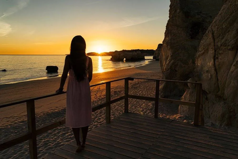 Woman looking out at a beach sunset in the Algarve — Shutterstock