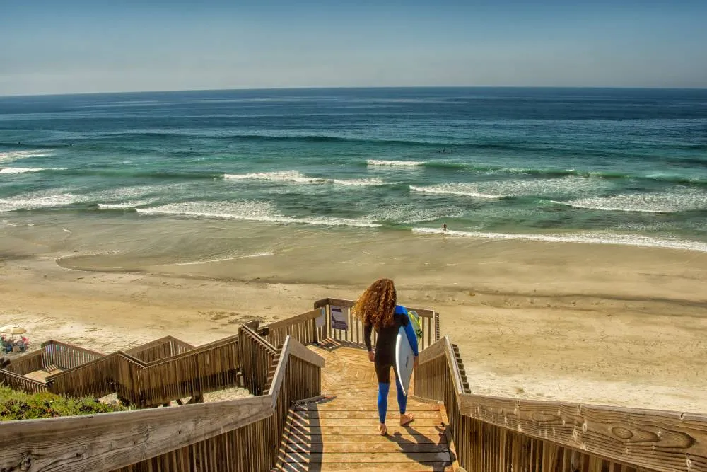 Szörfös sétál le a sétány lépcsőin a strand felé - Getty Images