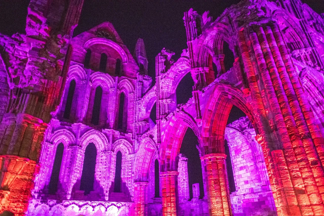 The eerie ruins of Whitby Abbey silhouetted against a dark sky, with spooky Halloween decorations and a foggy atmosphere.