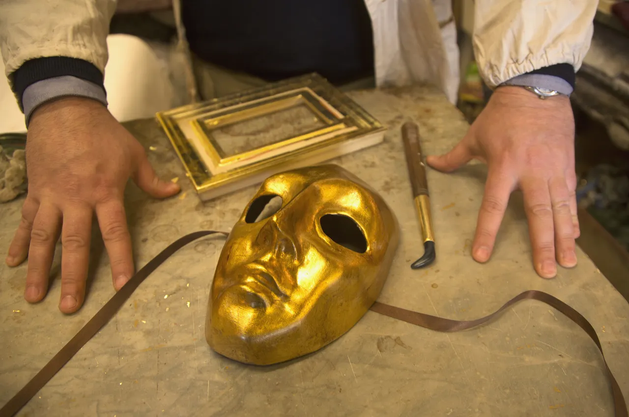Golden mask for sale with craftsman’s hand on table.