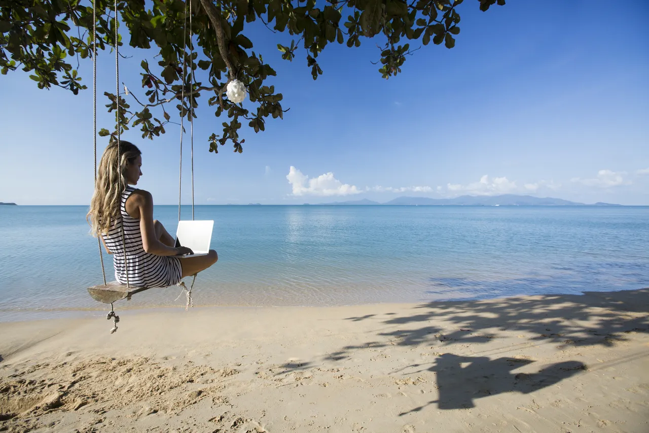 Woman working on laptop on beach, Thailand