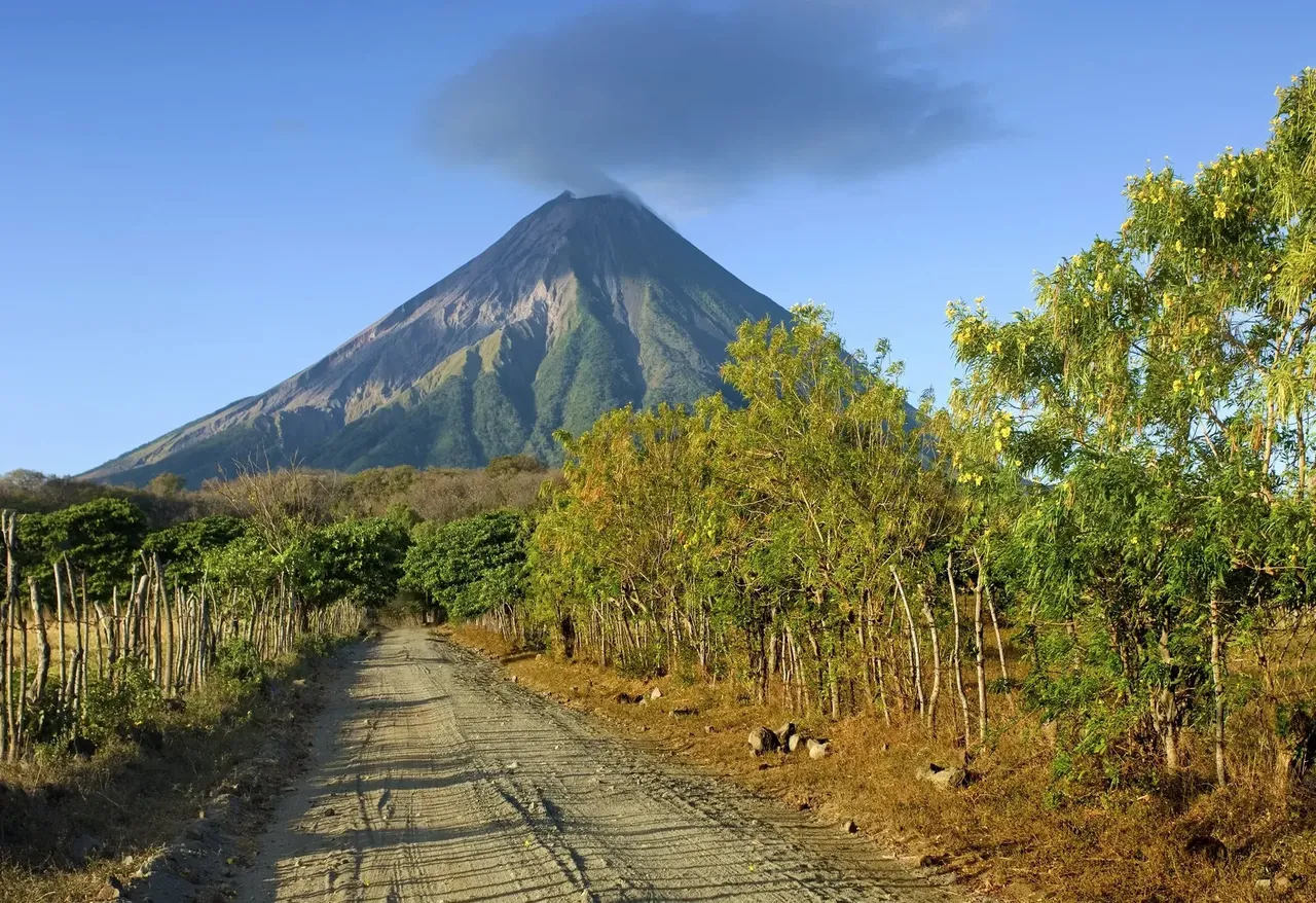 A peaceful dirt road on Ometepe Island, Nicaragua, winding through lush greenery with the majestic cone of a volcano rising in the background.