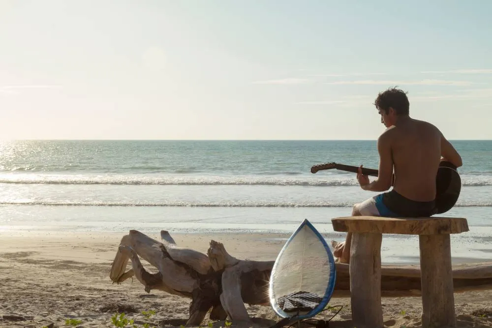 Surfer playing guitar on a tranquil beach — Getty Images