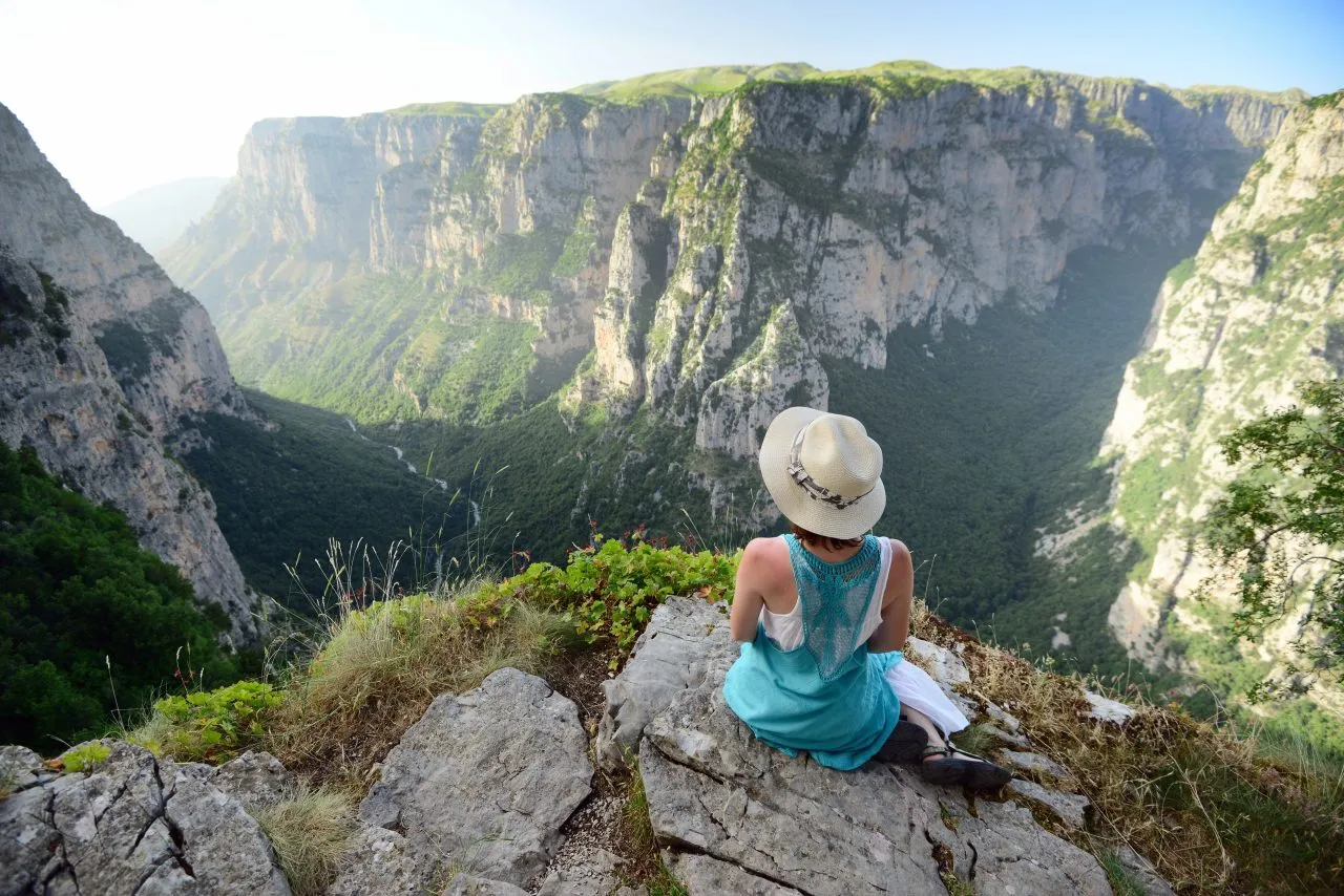 Young woman with blue dress and hat sitting over Vikos gorge, Timfy mountain, Zagoria / Epirus, Greece