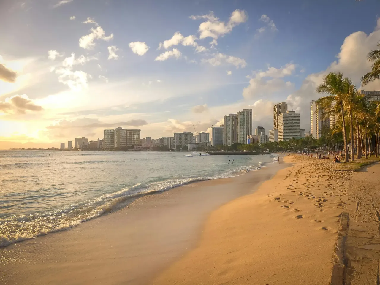 A scenic view of Waikiki Beach in Honolulu, Hawaii, with turquoise waters, surfers riding waves, and high-rise hotels along the shore.