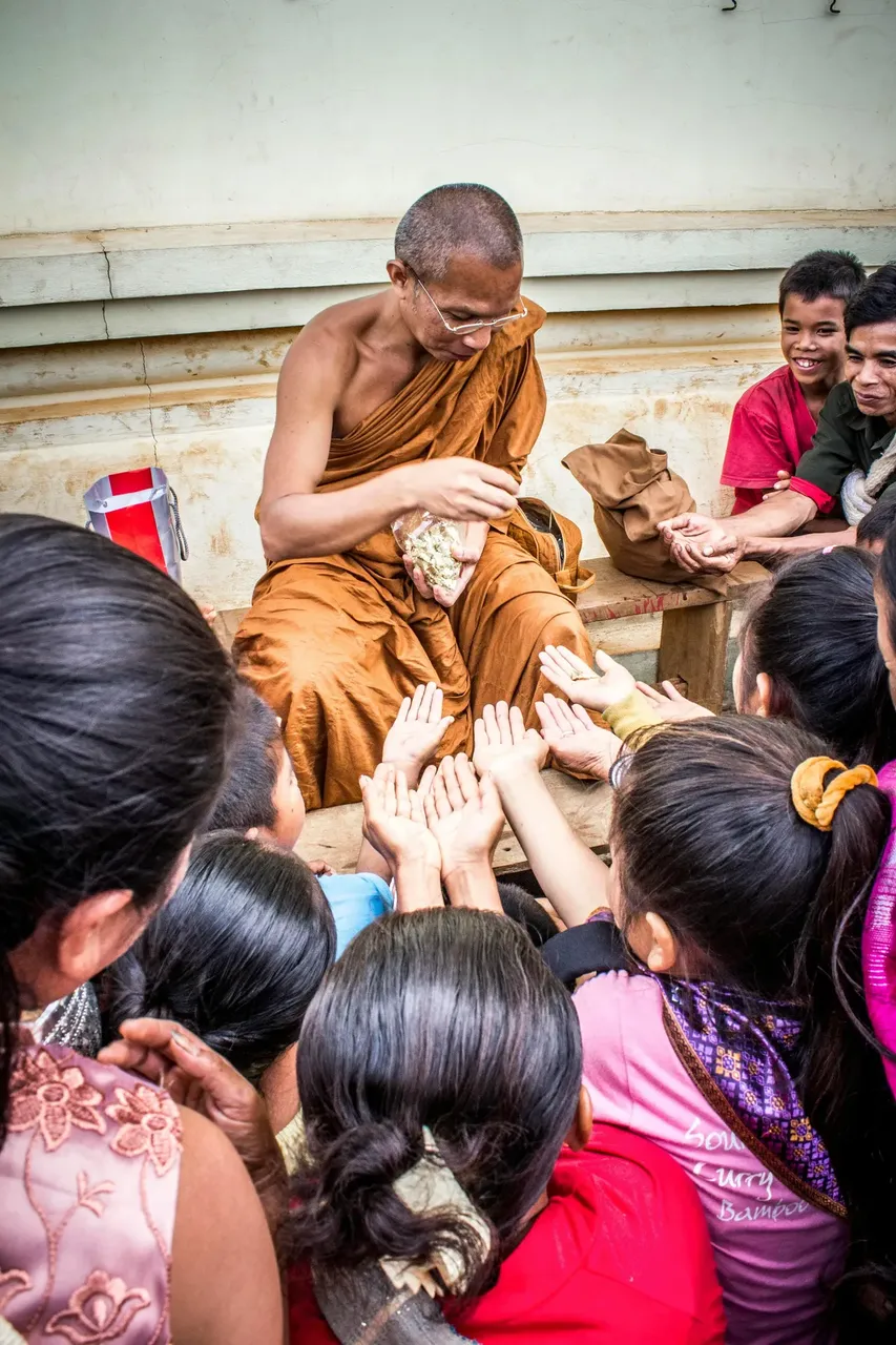 Un monje vestido con una túnica naranja ofrece comida a unos niños en Laos.