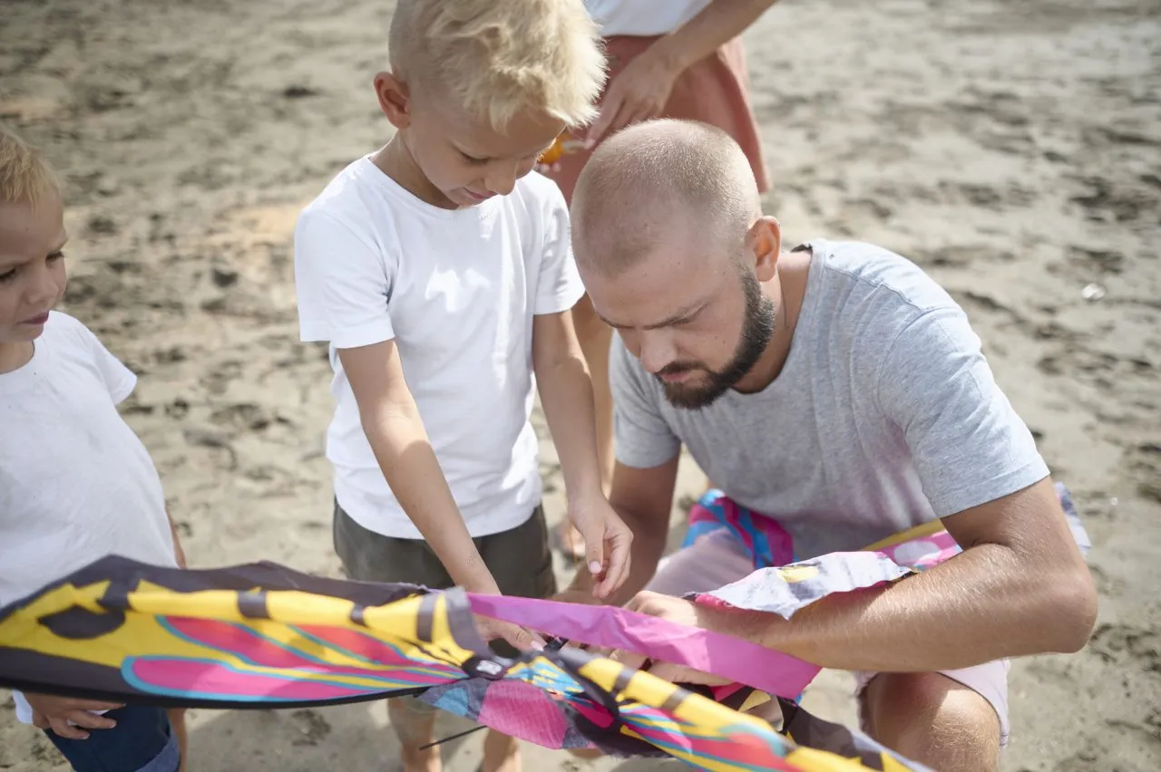 Father preparing kite with sons on the beach