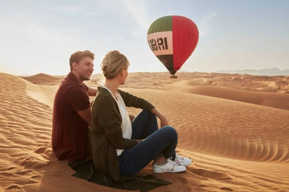 Couple in desert near Dubai with hot air balloon in background — Visit Dubai