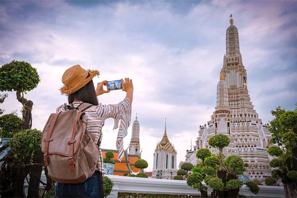 Woman taking a photo of the Wat Arun temple in Bangkok — Shutterstock