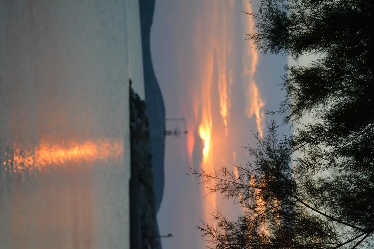 A breathtaking sunset in Tilos, Greece, with the sun dipping below the horizon, casting warm golden hues across the sky and sea