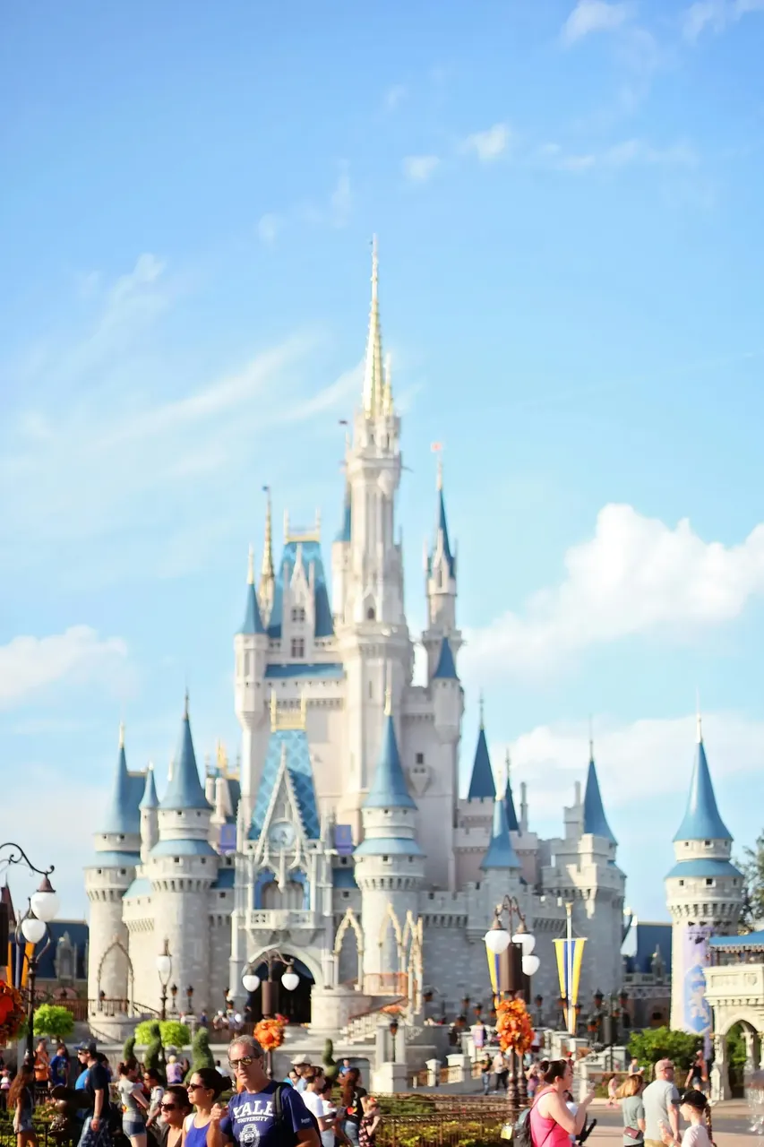 Cinderella’s Castle at Walt Disney World in Orlando, featuring towering blue spires, white stone walls, and golden accents, surrounded by lush greenery and a bright blue sky
