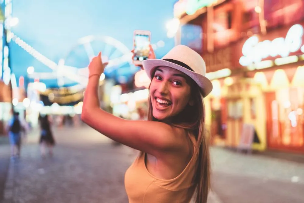 Woman near fairground at dusk filming with phone — Getty Images