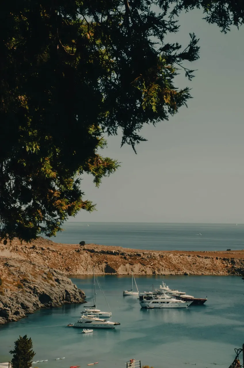 A picturesque view of Rhodes bay, with turquoise waters lapping against a sandy beach and boats anchored in the distance