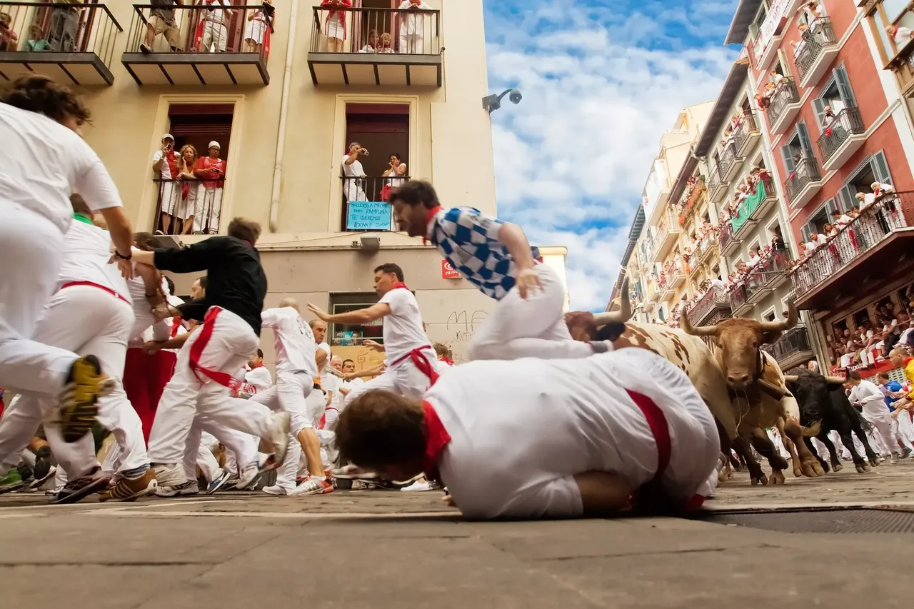 Crowds of men charging round a street corner in front of bulls, with one man on the ground in the foreground — Shutterstock