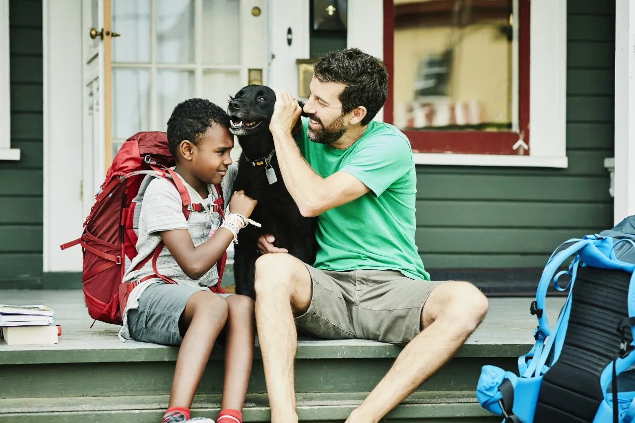 Father and son sitting on front porch of home with dog before going on backpacking trip