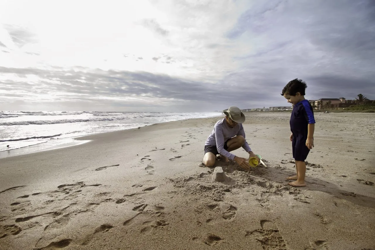 Grandfather playing with male child, beach, sand