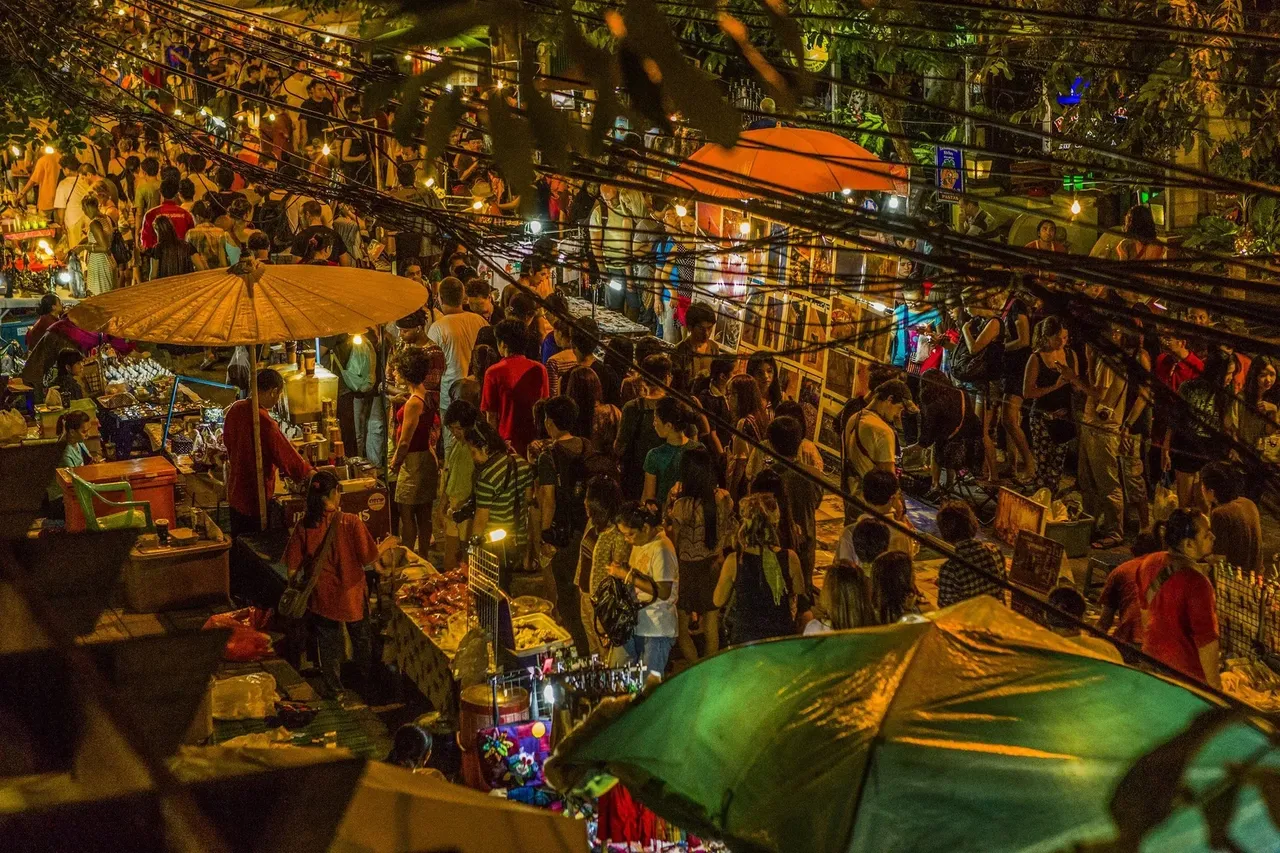 A vibrant and bustling street filled with colorful stalls, vendors, and crowds of people shopping and enjoying the lively atmosphere of the Chiang Mai Night Bazaar.