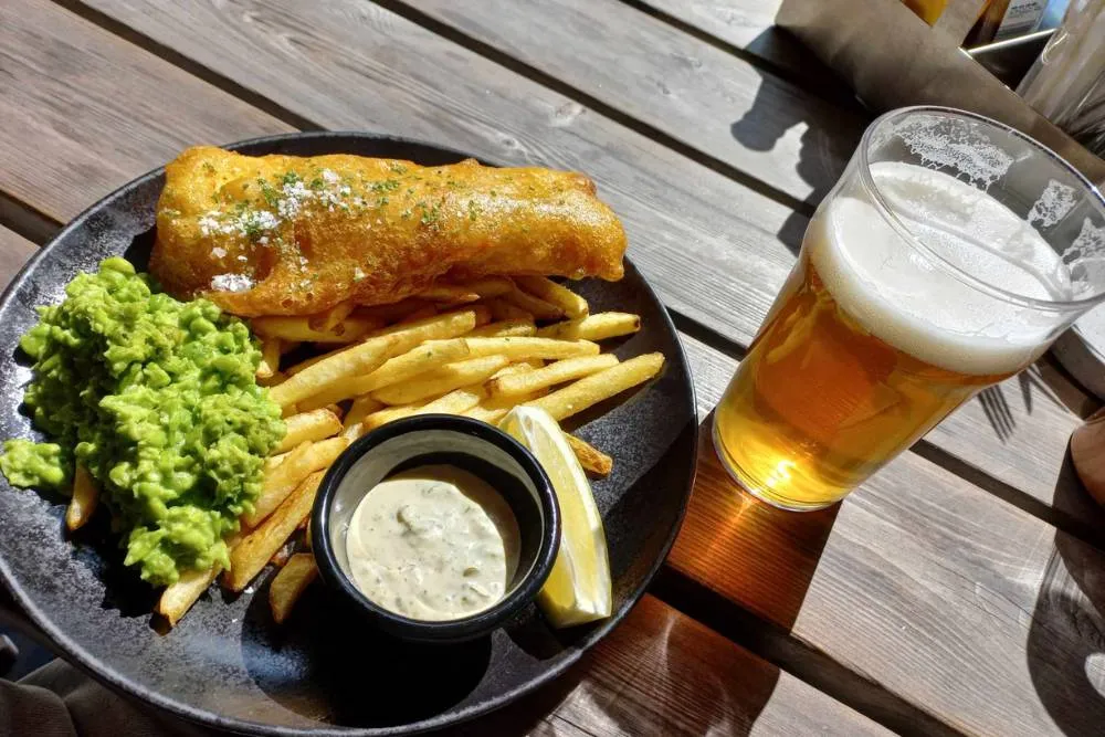 Fish and chips with garnishes on a plate with pint of beer — David Szmidt
