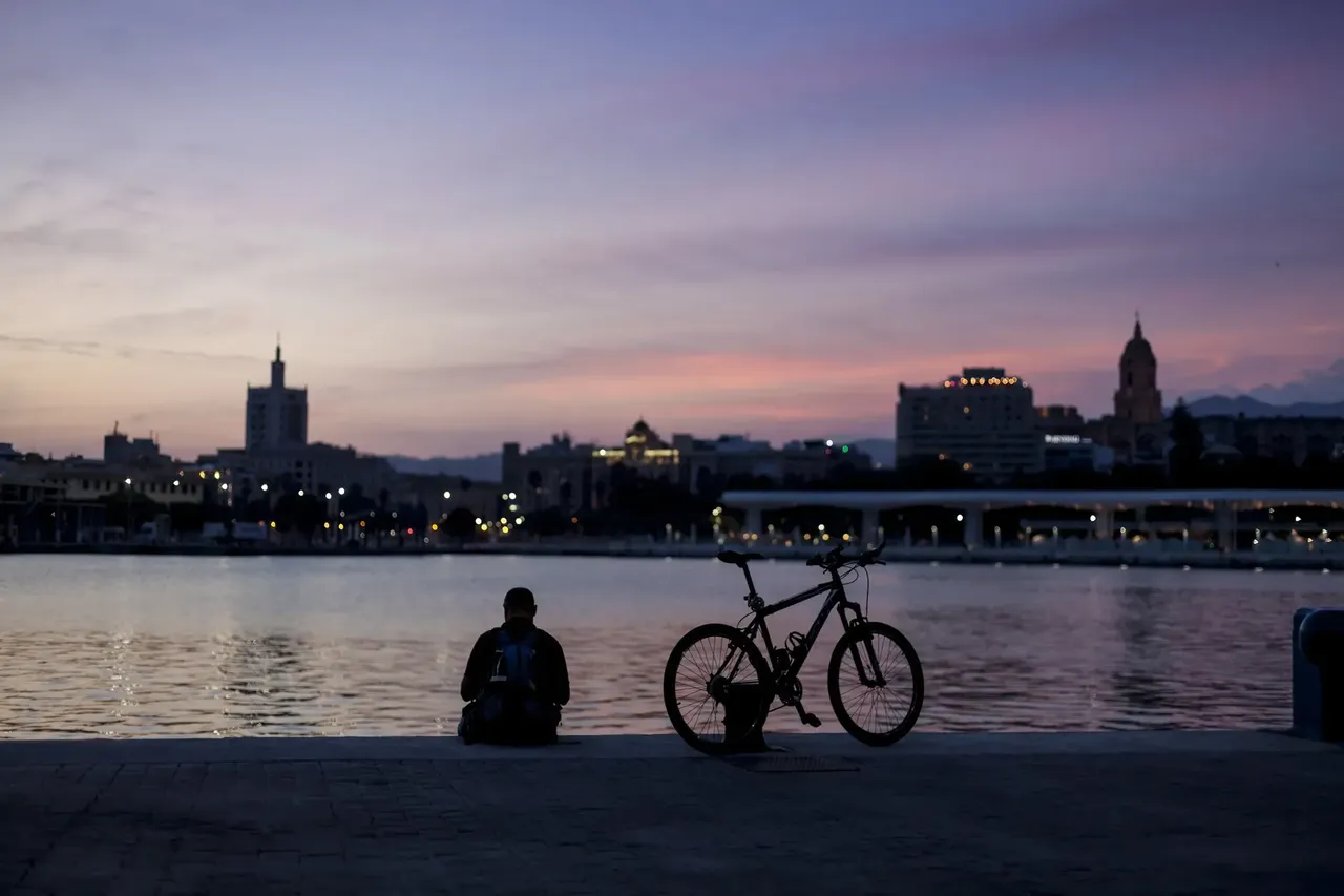 Seated tourist, watching the sunset in the port of Malaga. There’s a bike next door. Malaga, Andalucia, Spain