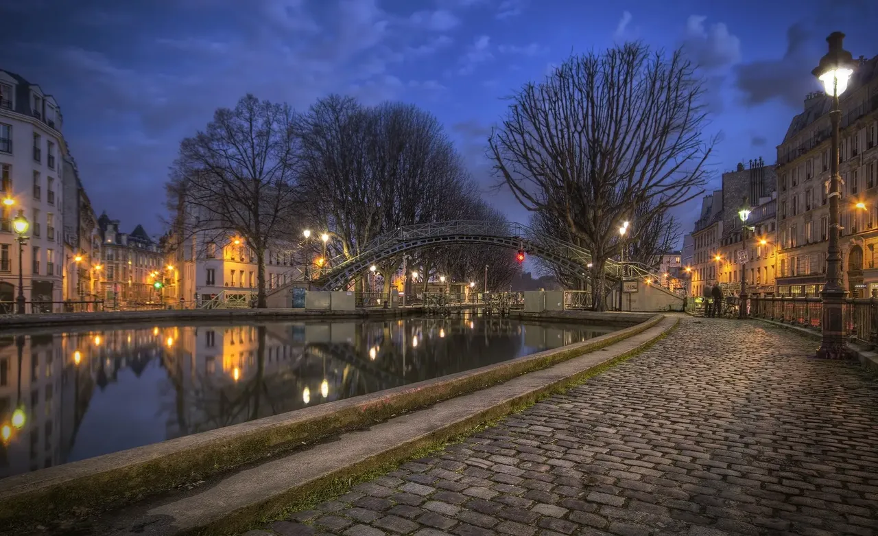 A serene nighttime view of Canal St. Martin, with reflections of lights dancing on the water and quiet streets lining the canal.