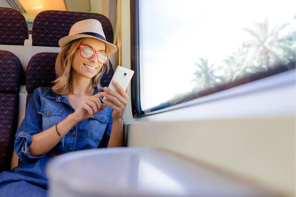 Woman sat by window on a train looking at smartphone and smiling — Shutterstock